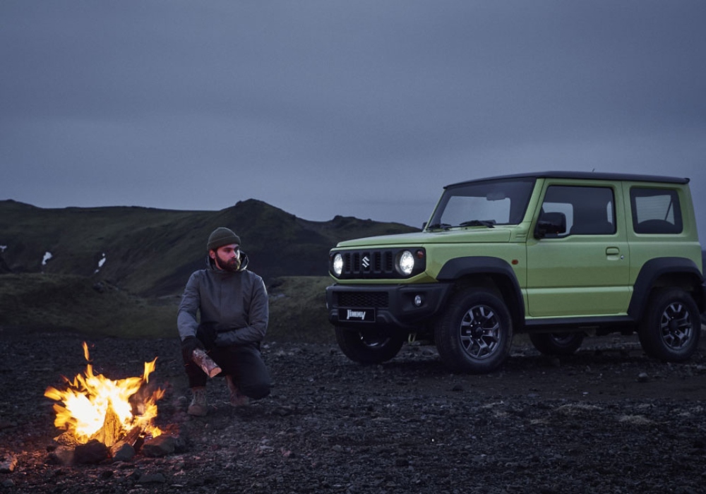 Suzuki Jimny verde oliva estacionado en un terreno volcánico.